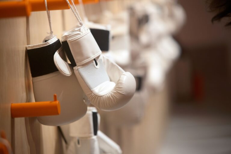 Close-up of white boxing gloves hanging neatly on an orange hook indoors.